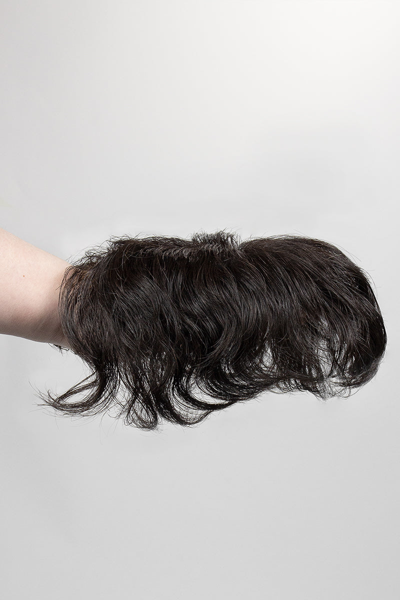 Hair topper held by a hand against a plain background