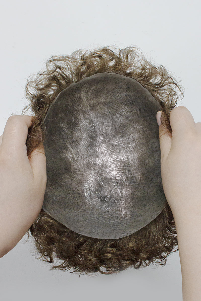 Person holding a bald cap with curly hair on a plain background