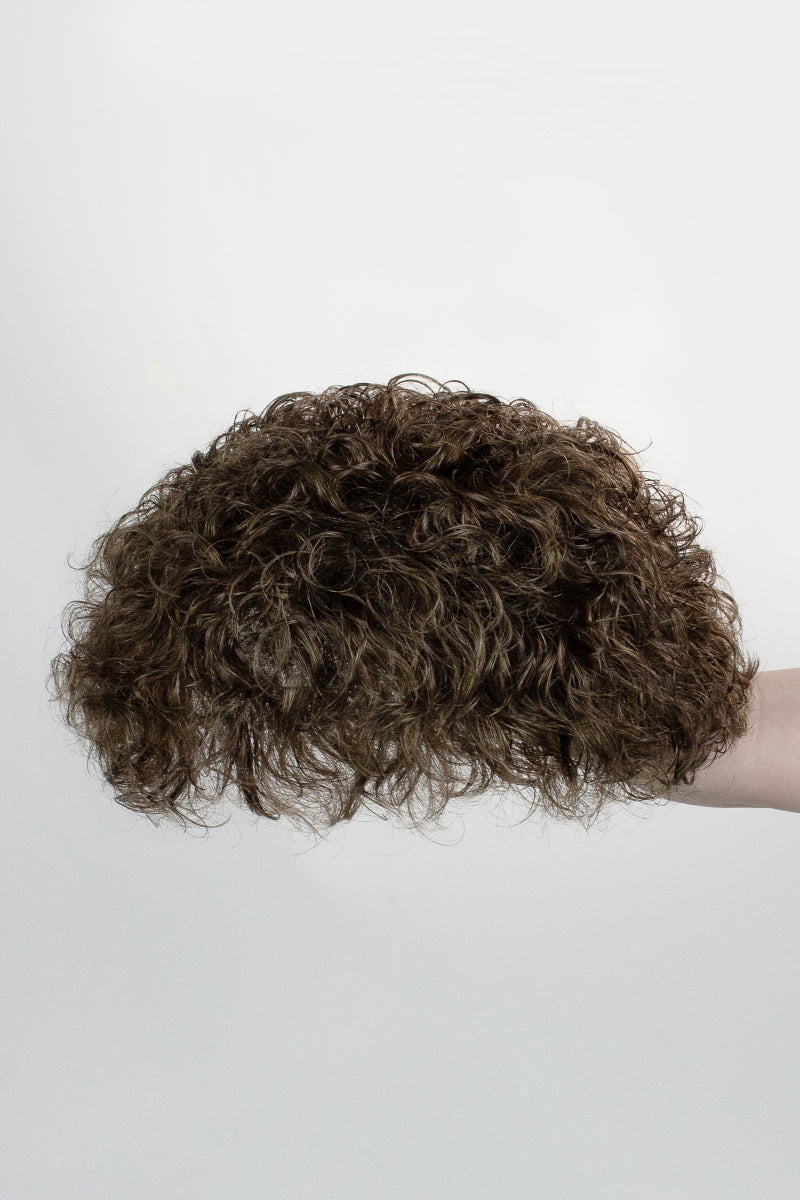 Curly brown hairpiece held by a person against a white background